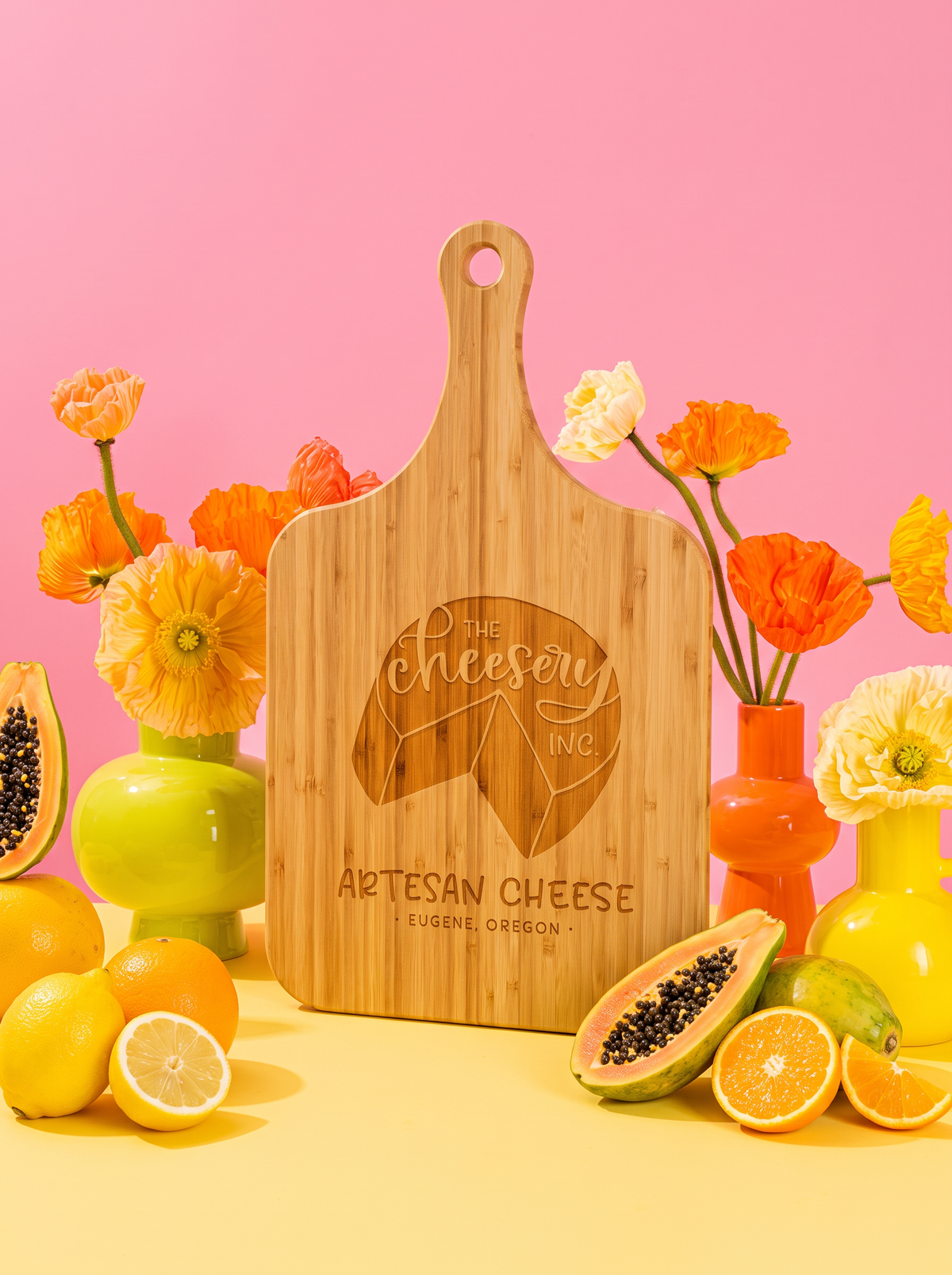 Custom logo engraved on a bamboo handle cutting board, styled with colorful flowers against a pink background.