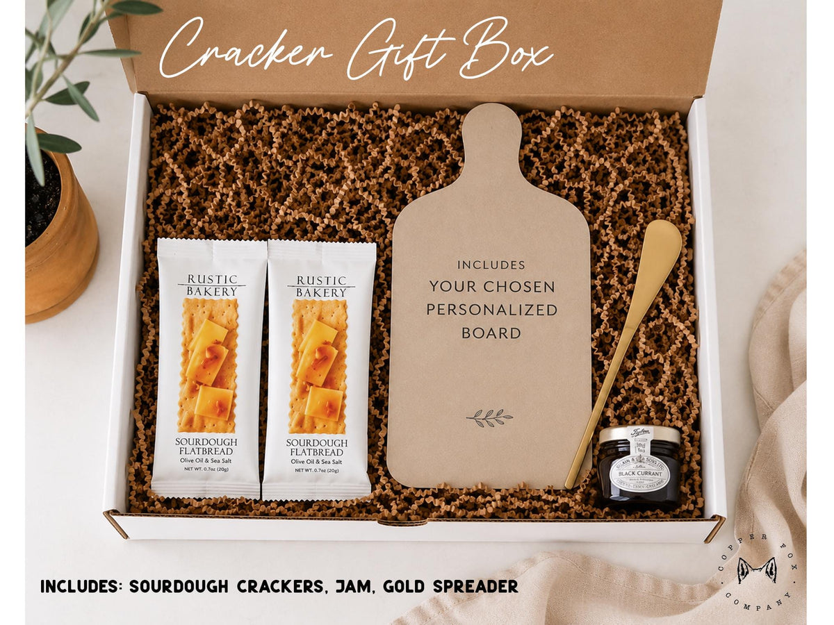A gift box containing various items, including two packages of flatbread crackers, a wooden cutting board, a jar of jam, and a knife.