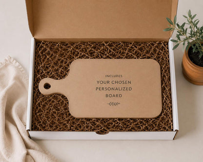a cardboard box containing a wooden cutting board, with a potted plant and a cloth visible in the background.