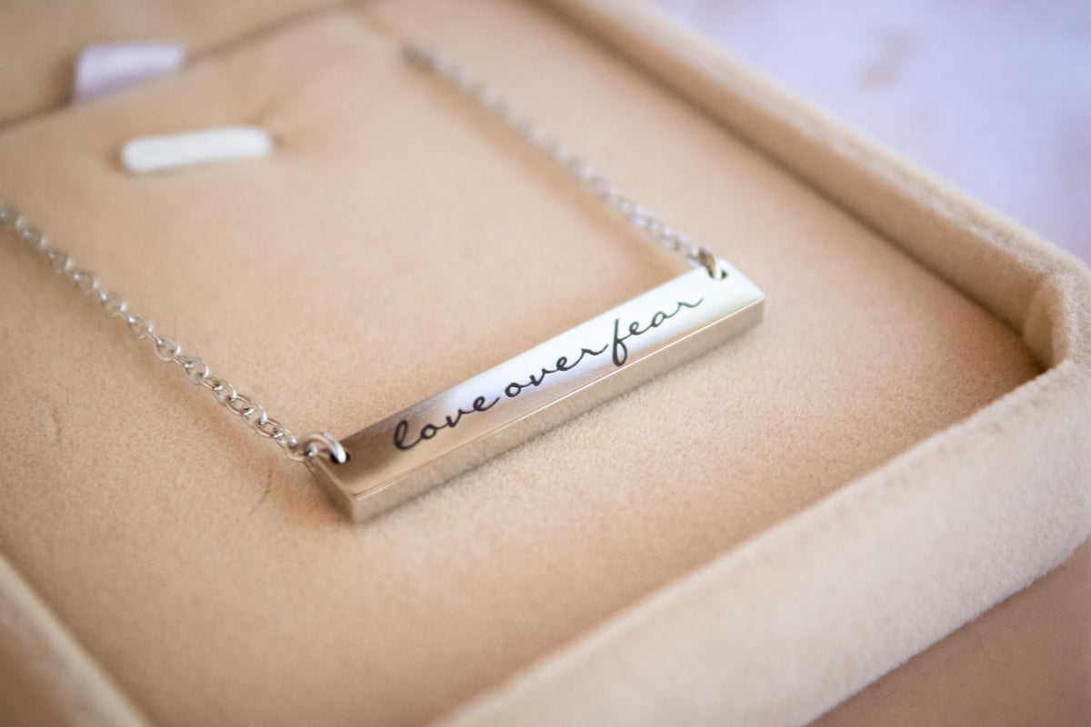 A necklace with a rectangular pendant that says "love over fear".