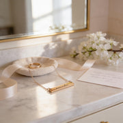 a gold necklace with a pendant, a ring, and a bouquet of white flowers on a marble countertop.