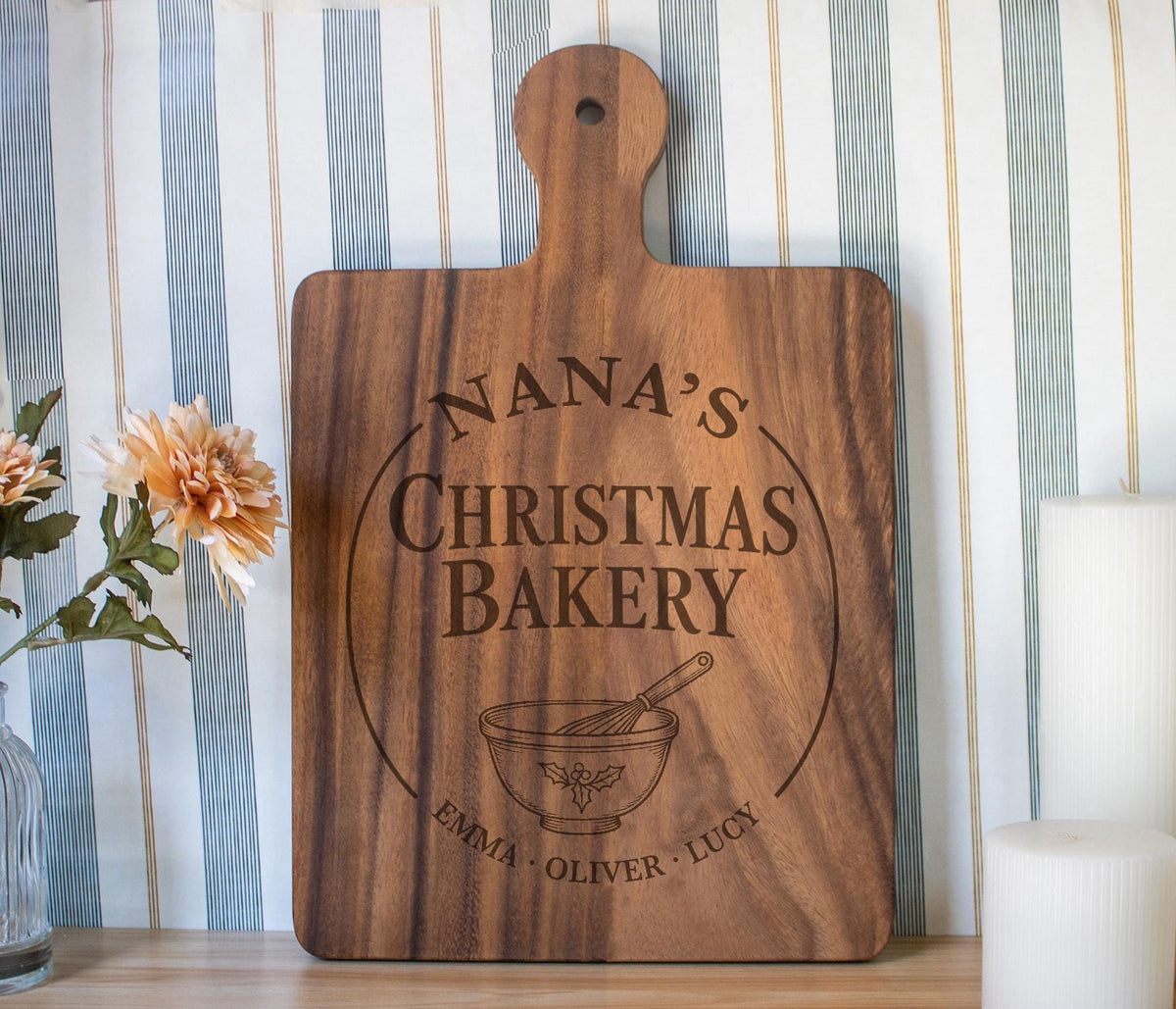 Holly Mixing Bowl edited mockup on a large dark wooden paddle board, showing Nana’s Christmas Bakery and grandkids’ names against striped wallpaper.