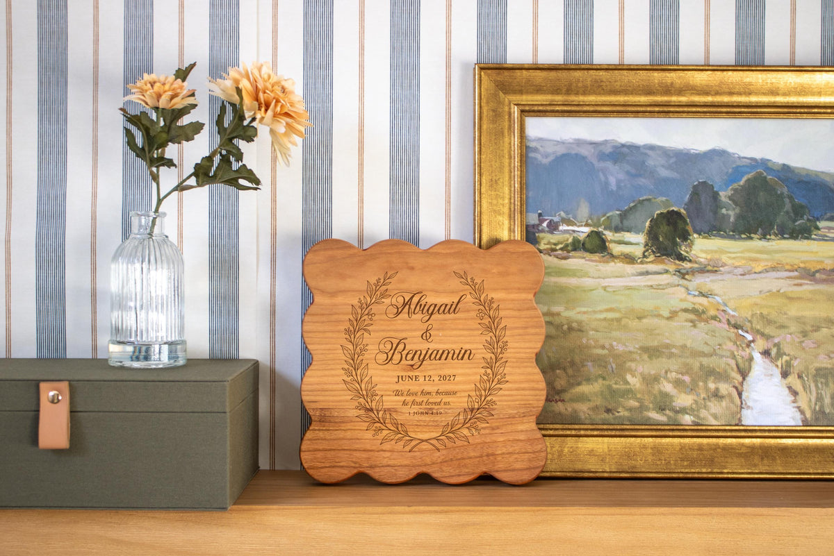 Edited mockup of first loved wreath on a light-colored scalloped square board beside a framed landscape.