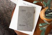 Gray Garden Hydrangea journal mockup on a book beside a potted plant. Cover shows a hydrangea, Garden Observations, Julia Bennett, and Field Notes.