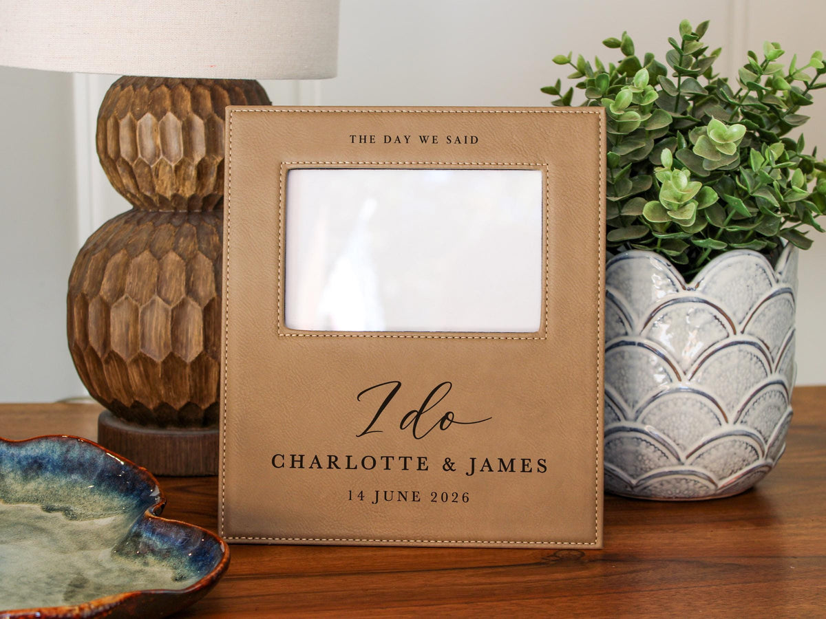 I Do frame mockup beside a lamp and a potted plant, with an empty photo opening. THE DAY WE SAID above the opening; I do, Charlotte & James and 14 June 2026 below.