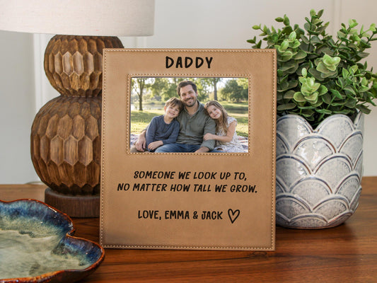 Edited mockup of the tall we grow Daddy frame beside a lamp and plant, with a sample dad-and-children photo, engraved saying, Love, Emma & Jack signature and outline heart.