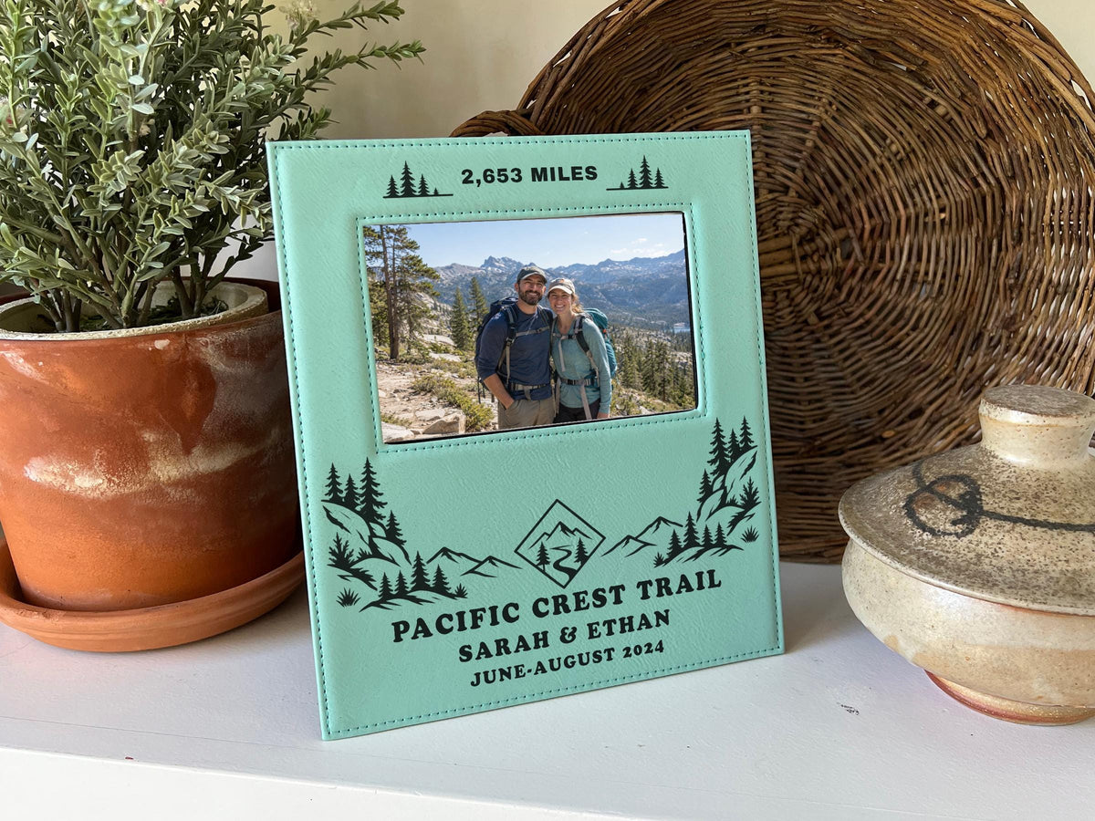Edited mockup of the Pacific Crest Trail frame beside a plant and woven tray, with trail artwork, sample names and date, and an illustrative hiking couple photo.