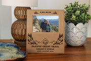 Edited mockup of the Pacific Crest Trail frame on a wooden table, showing sample mileage, names and date around an illustrative hiking couple photo.