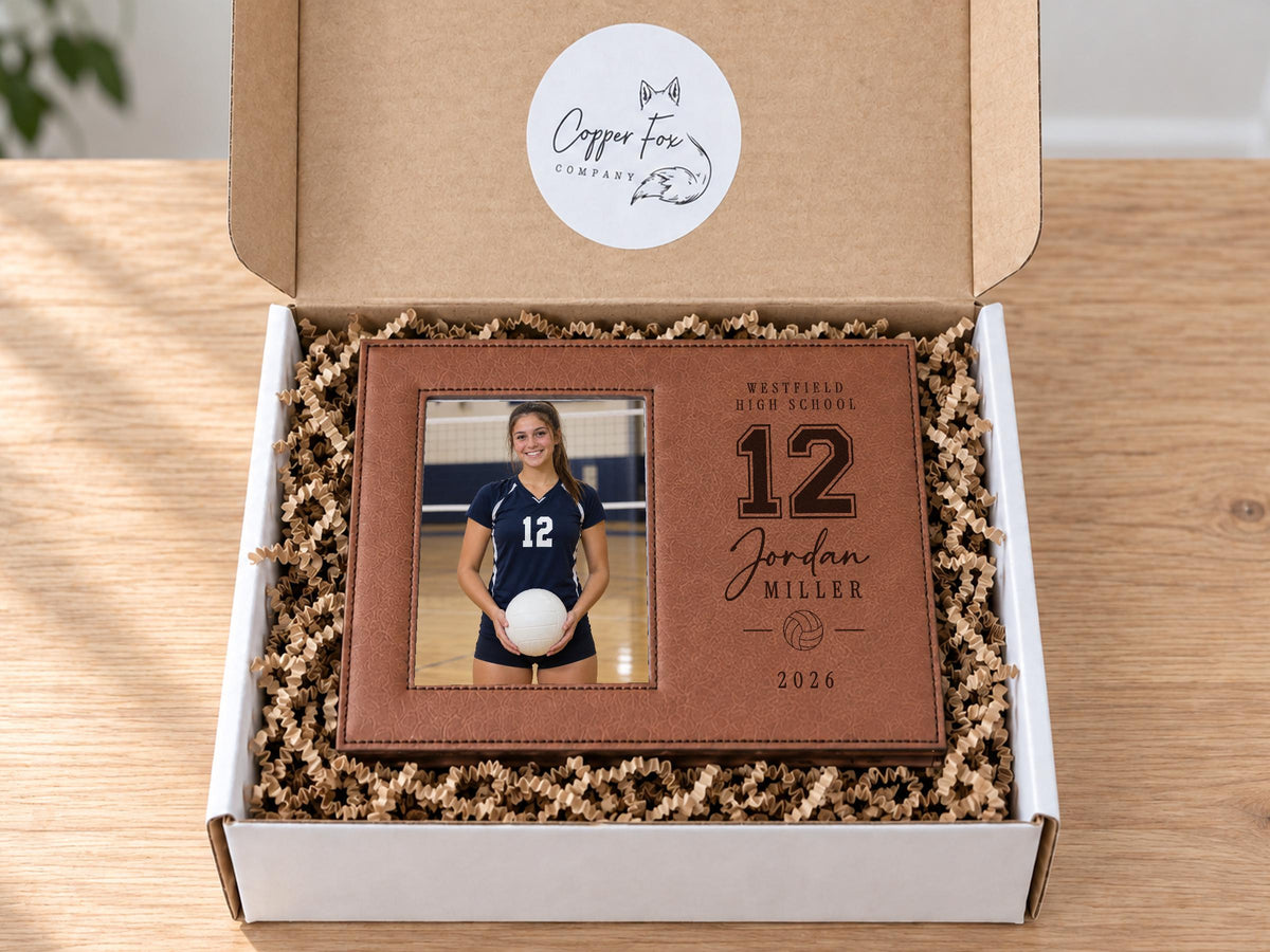 Edited Varsity Volleyball frame mockup in an open gift box with crinkle paper, showing an illustrative volleyball player portrait and personalized number, name, school and year.