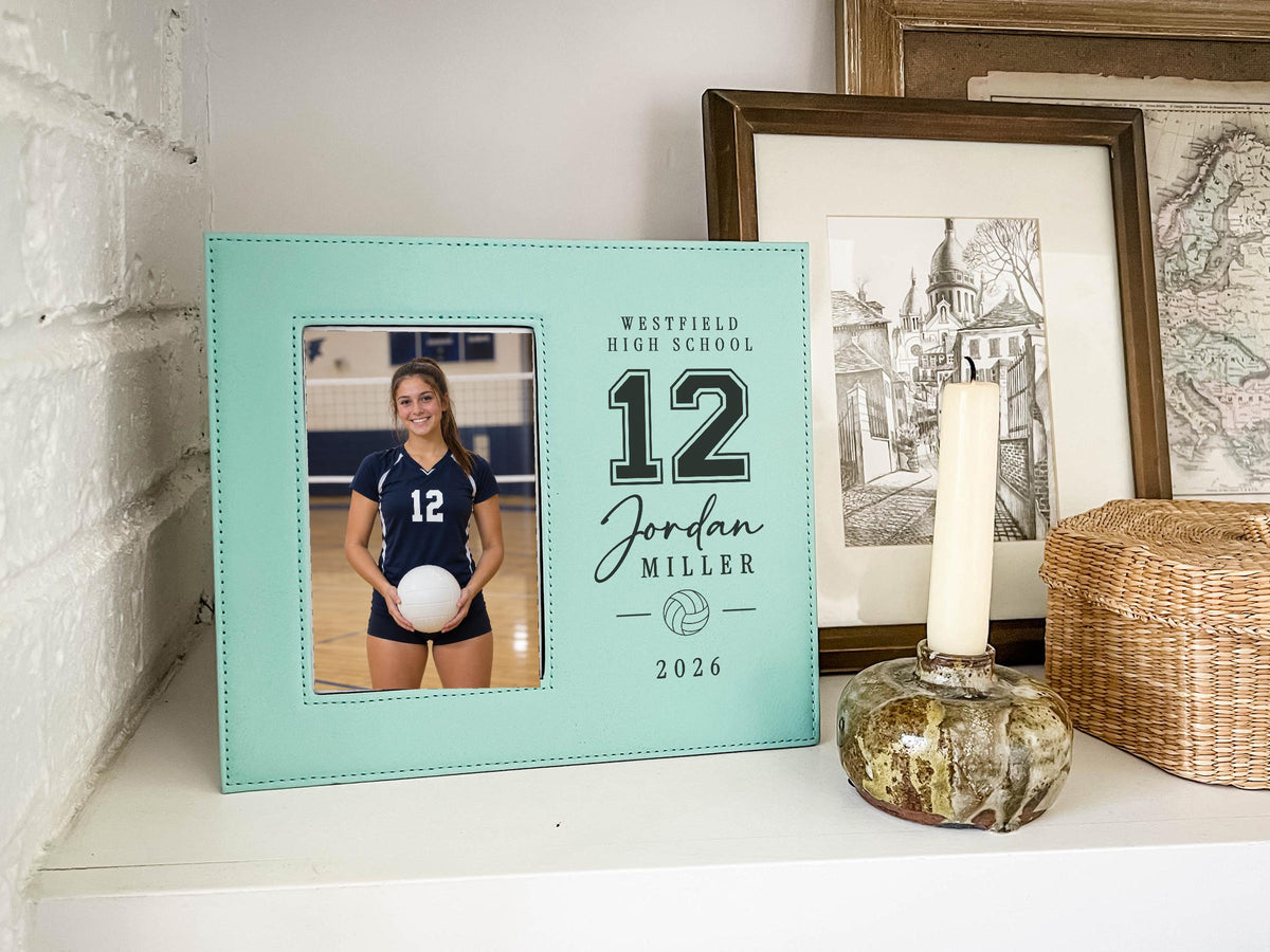 Edited teal Varsity Volleyball frame mockup on a shelf beside a candle and framed art, with an illustrative player portrait and personalized varsity number, name, school and year.
